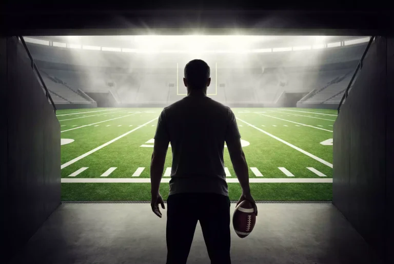 Person hält einen American Football und schaut auf ein Stadionfeld