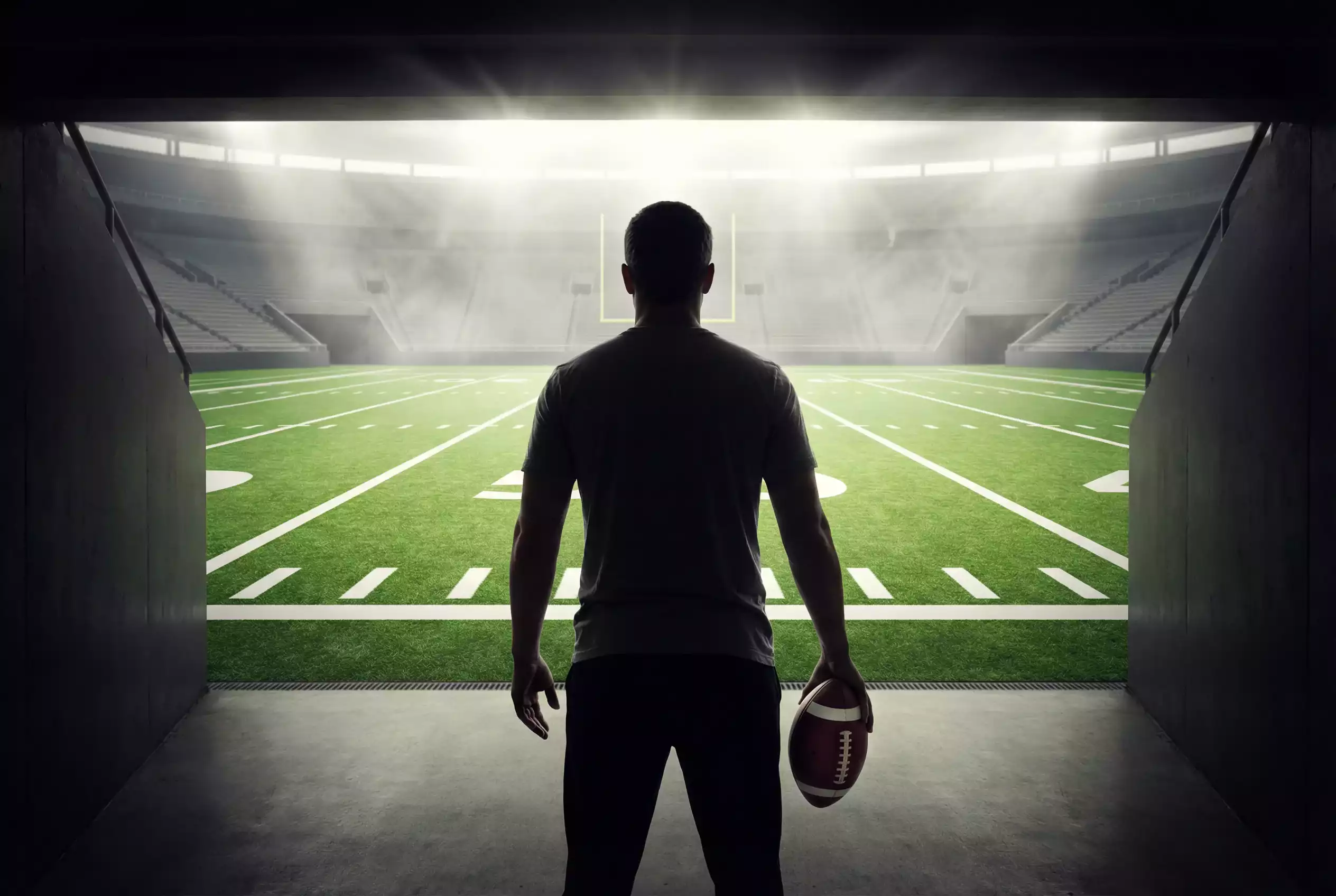 Person hält einen American Football und schaut auf ein Stadionfeld